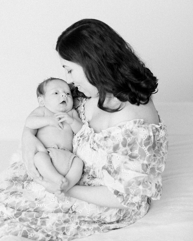 Mom in neutral-toned dress cradles her newborn in arms, natural light gently highlighting their close bond.