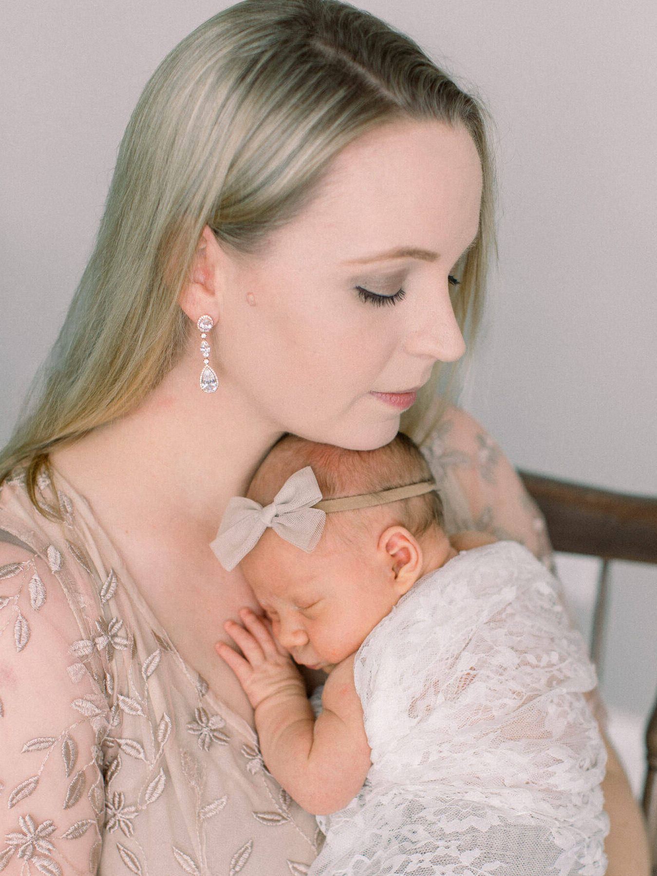 Elegant portrait of mother in curated wardrobe holding her baby close in classic studio setting, neutral palette.