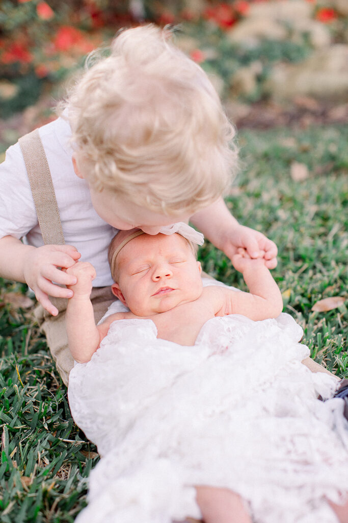 Big brother and baby sister pose outdoors with their family’s black Labrador during a newborn photo session.