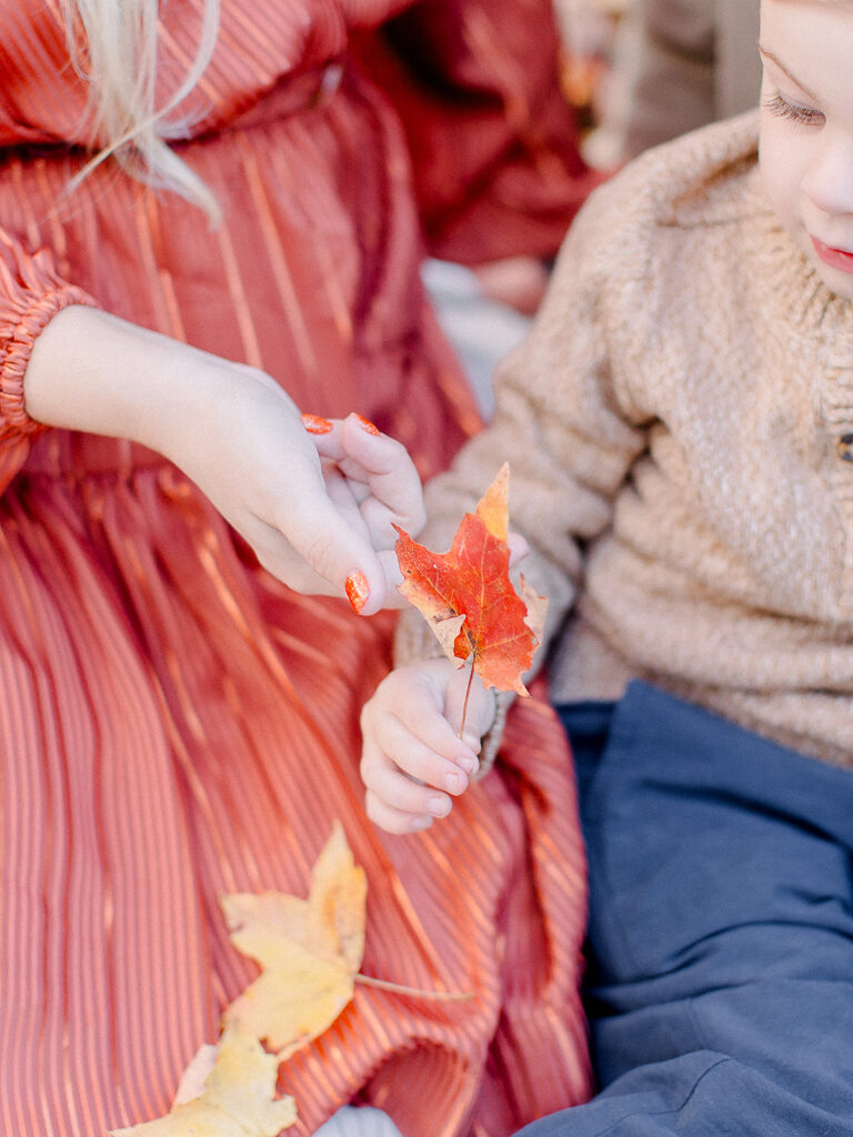 Child handing freshly fallen autumn leaves to his mother, gathered for a fall craft for kids in New England