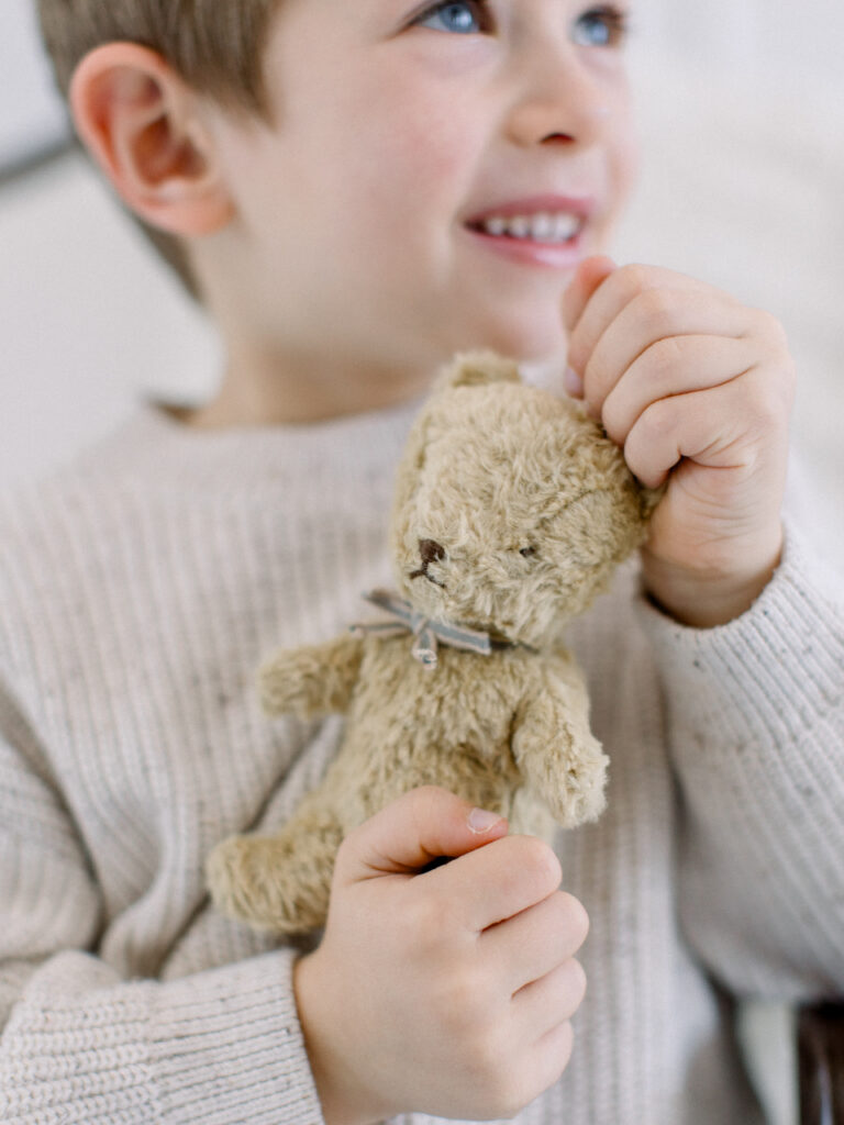 Closeup of little boy in a white sweater snuggling his teddy bear with a neutral background. Timeless child portraits in Massachusetts by Fieldstone Studio.
